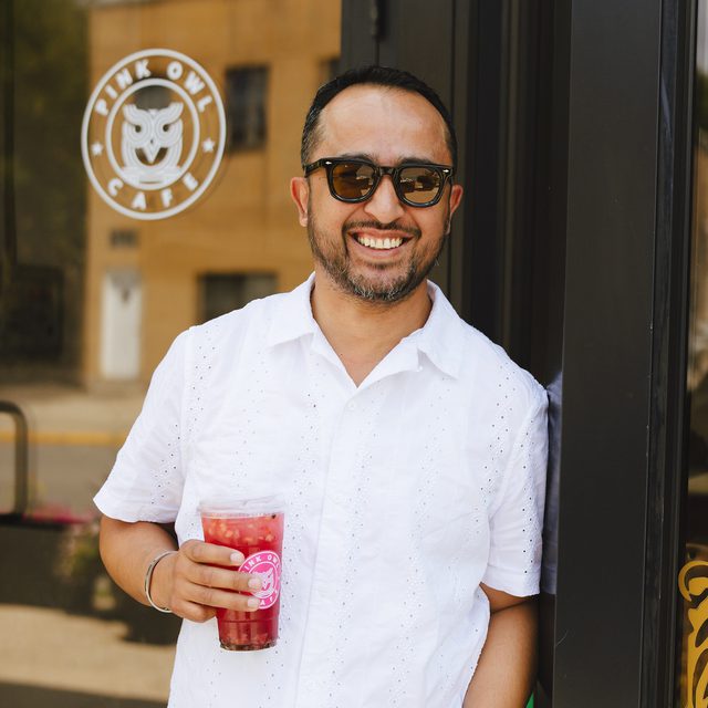 Alex Herrera in the doorway of the cafe holding a strawberry refresher